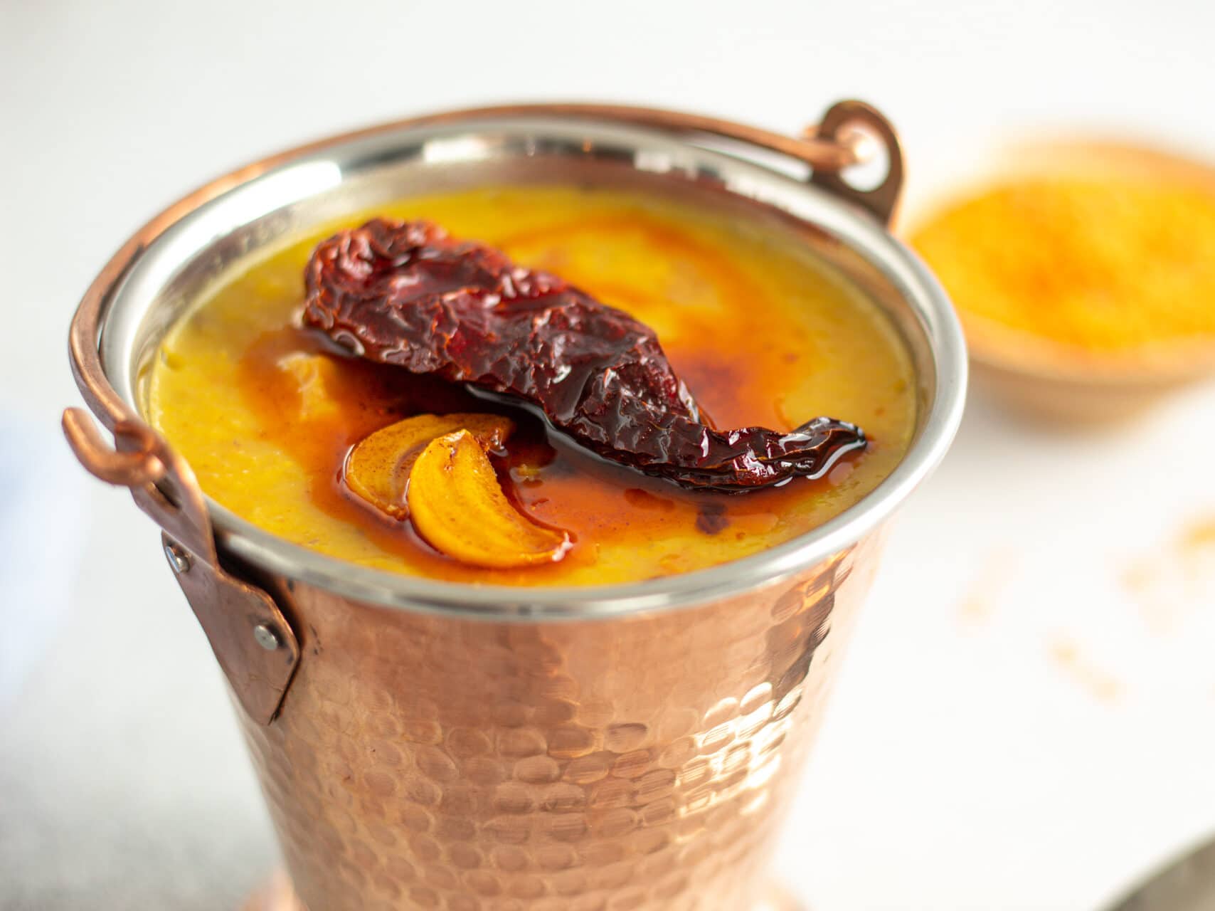 red lentils in a copper bucket with dried red chili and garlic slices with oil on top